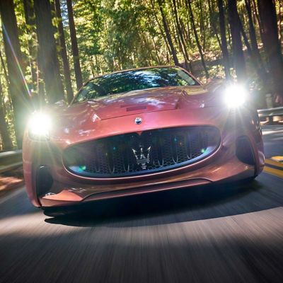 Maserati Granturismo front view, running during the day with headlights on under a tree-lined street