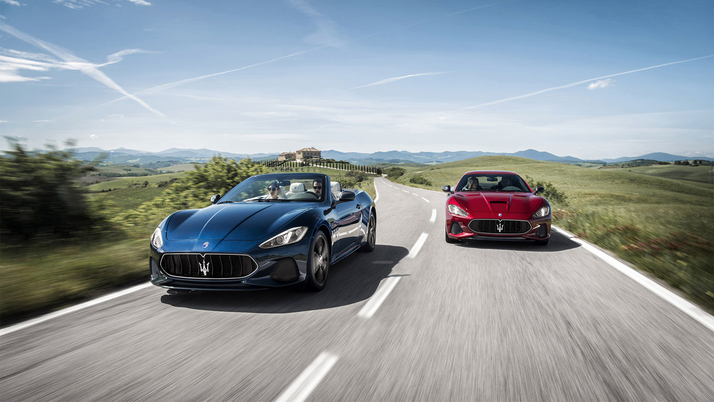 Roter und blauer Maserati GranTurismo und GranCabrio fahren durch eine schöne Landschaft
