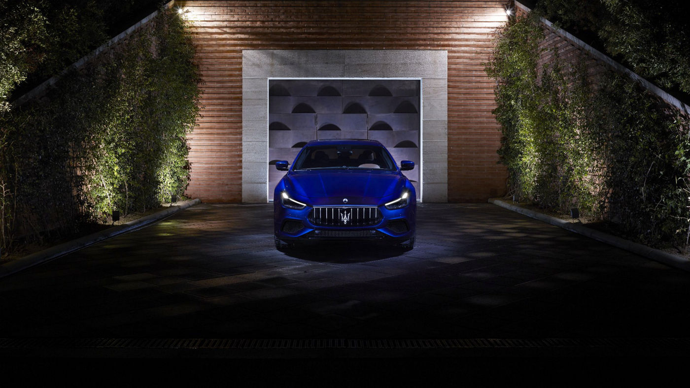 Maserati Ghibli S Q4 with its headlights lit - front view - greenery wall on the background