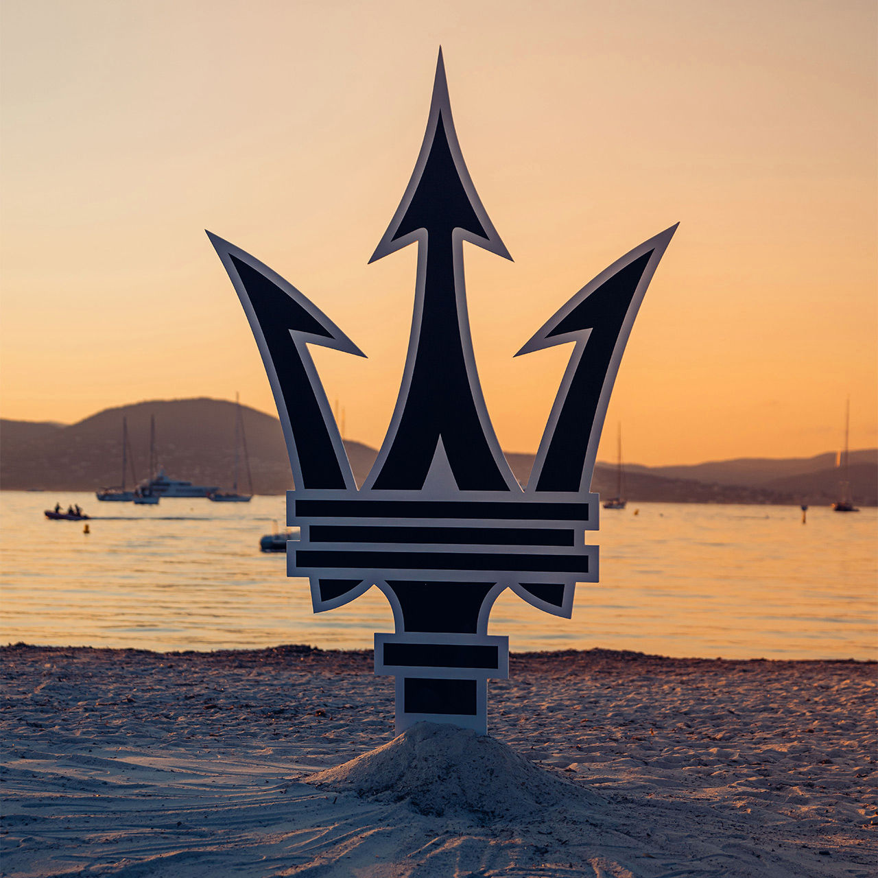 Logo de Maserati plantado en la playa de Saint Tropez en frente de una puesta de sol
