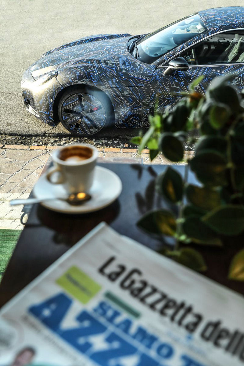 Periódico y taza de café encima de una mesa en frente del prototipo Maserati GranTurismo