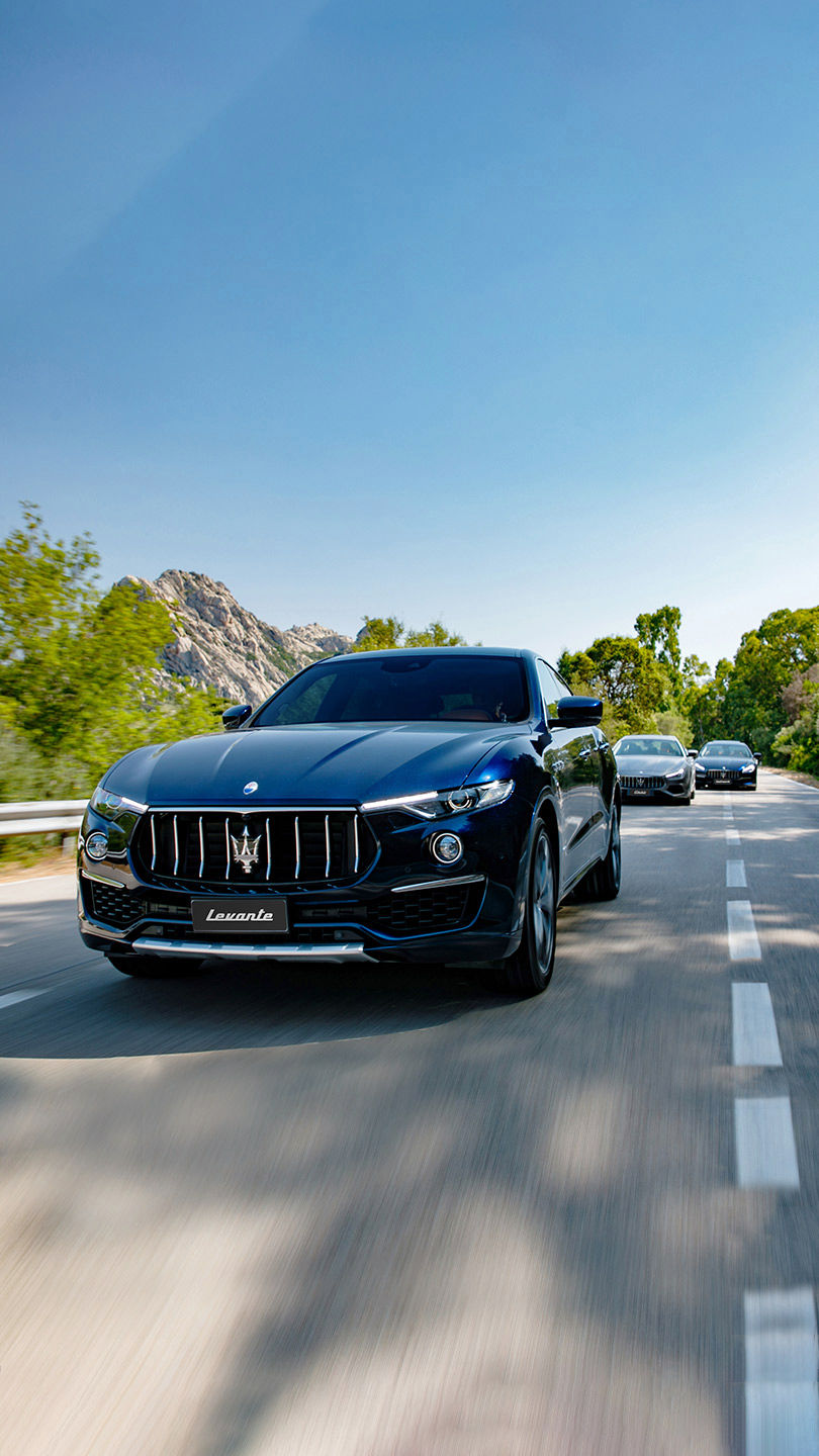 Blauer Maserati Levante fährt durch grüne Berglandschaft, zwei weitere Maseratis im Hintergrund