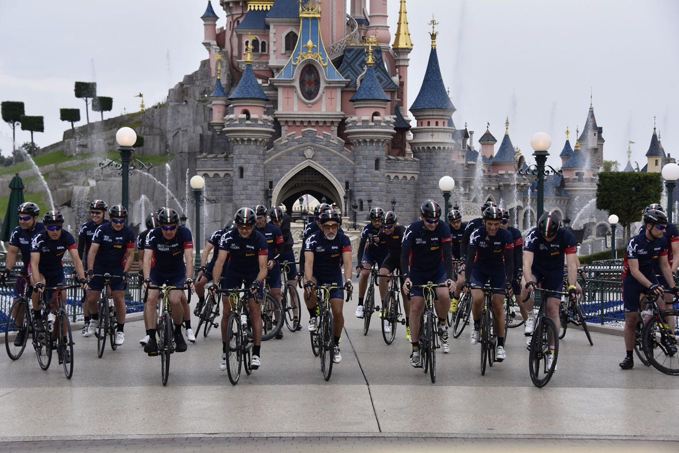 Ciclistas sobre bicicletas con ropa Maserati en frente del castillo de la Bella Durmiente en Disneyland