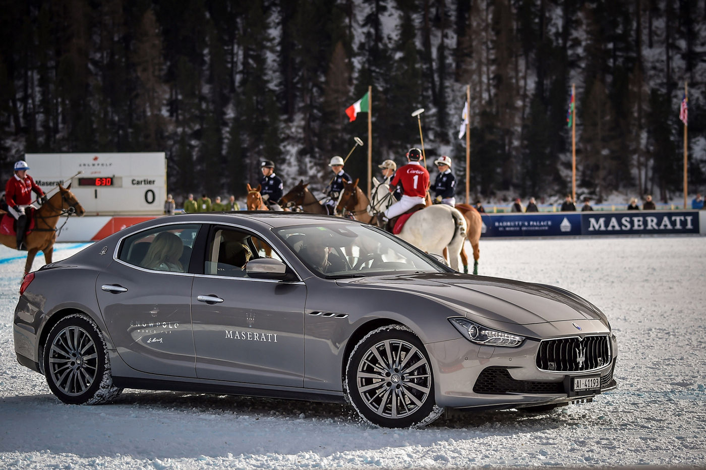 Jugadores de polo en fila dentro del campo en la nieve detrás de un Maserati