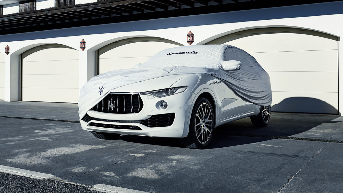 A Maserati-branded outdoor car cover draped on a white Maserati Levante.