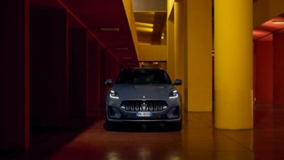 Front view of a gray colored Maserati Grecale Folgore luxury electric SUV in a modern garage with corridor painted in red and yellow