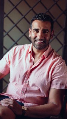 Rajvinder Bains seated at the table with a glass of red wine placed on the table mobile